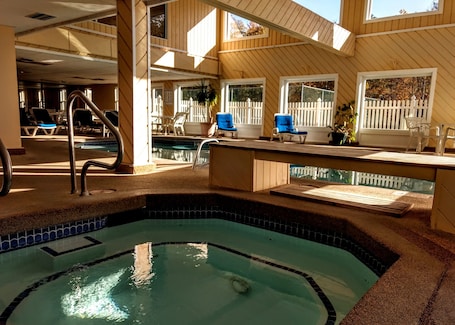 A pool area with a hot tub, lounge chairs, and a wooden deck.