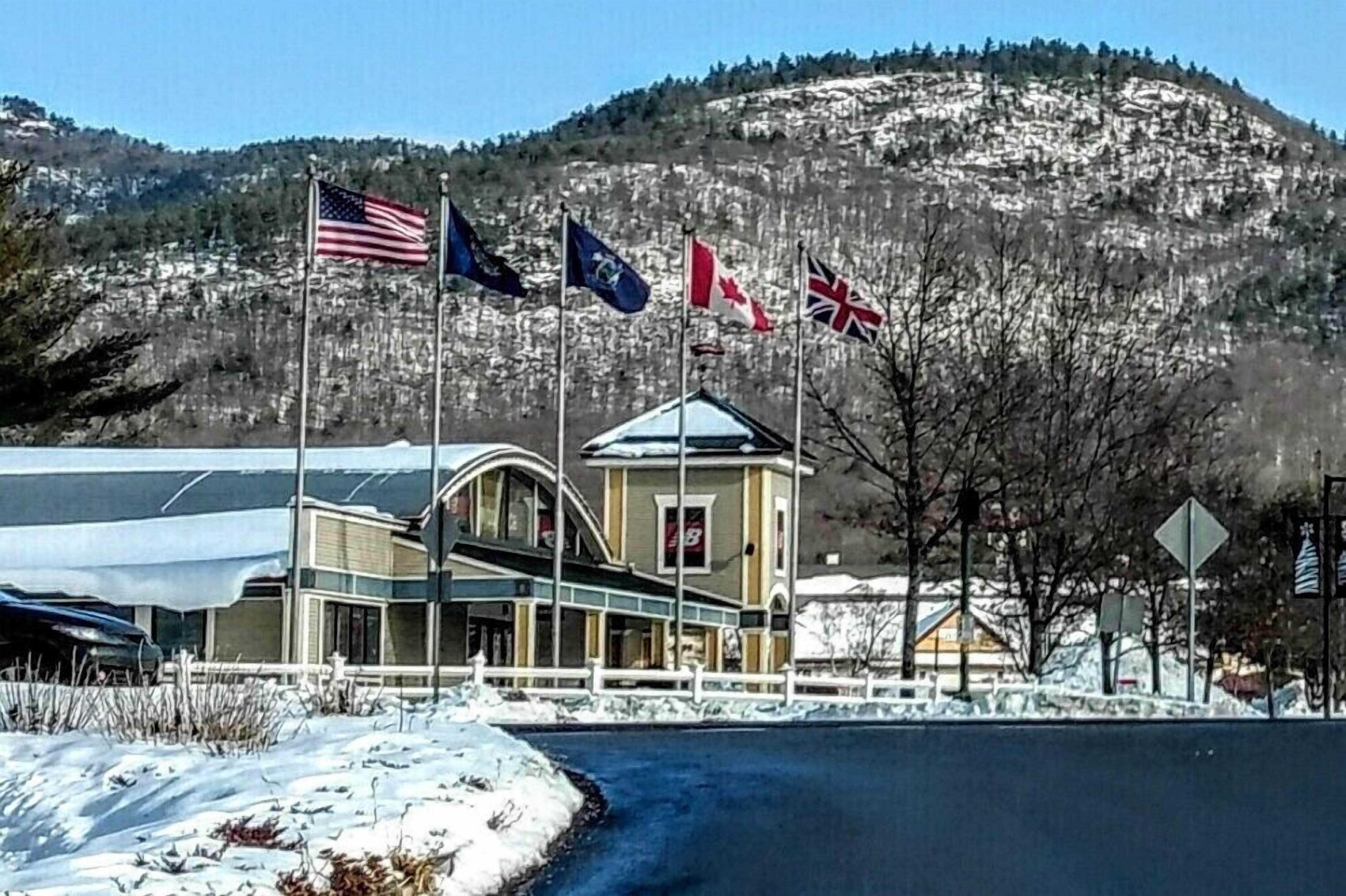 A building with multiple flags, a snow-covered landscape, and a mountainous backdrop.