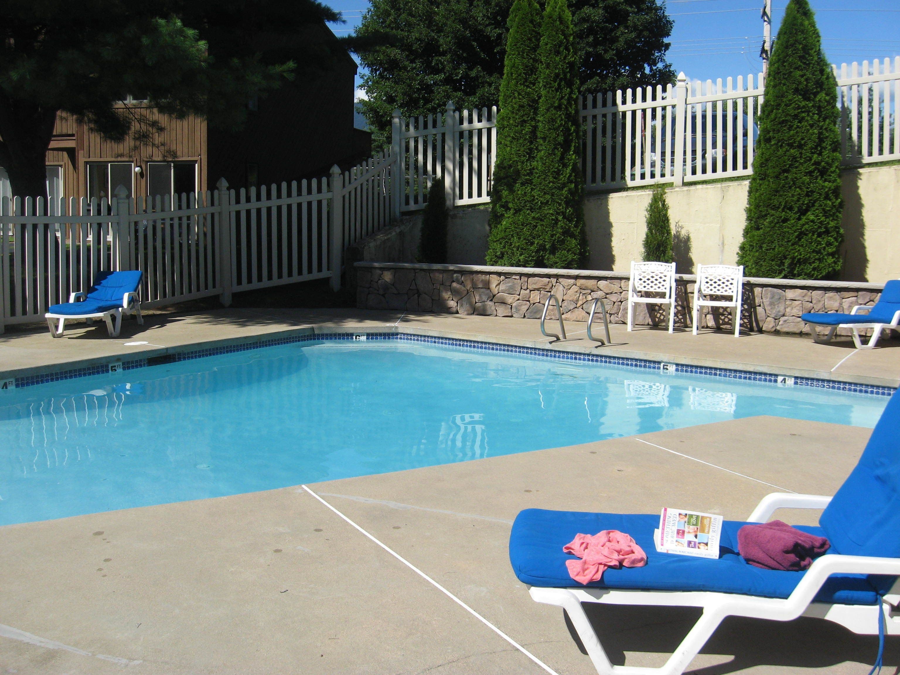 A swimming pool with blue tiles, surrounded by white lounge chairs and a stone wall.