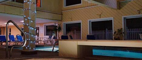 A pool area with a small pool, lounge chairs, and a staircase leading to an upper level.
