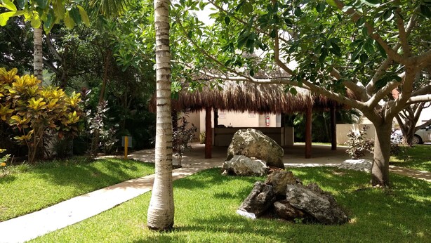 A well-maintained garden with a thatched-roof structure, large rocks, and various tropical plants. - Villas Narcisos (Cancun)