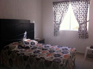 A bedroom with a bed, a TV, a window with patterned curtains, and a small white table.