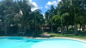 A swimming pool surrounded by palm trees and a clear sky. - Villas Narcisos (Cancun)