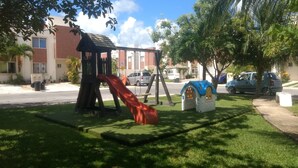A playground with a slide and swings, surrounded by grass and trees. - Villas Narcisos (Cancun)