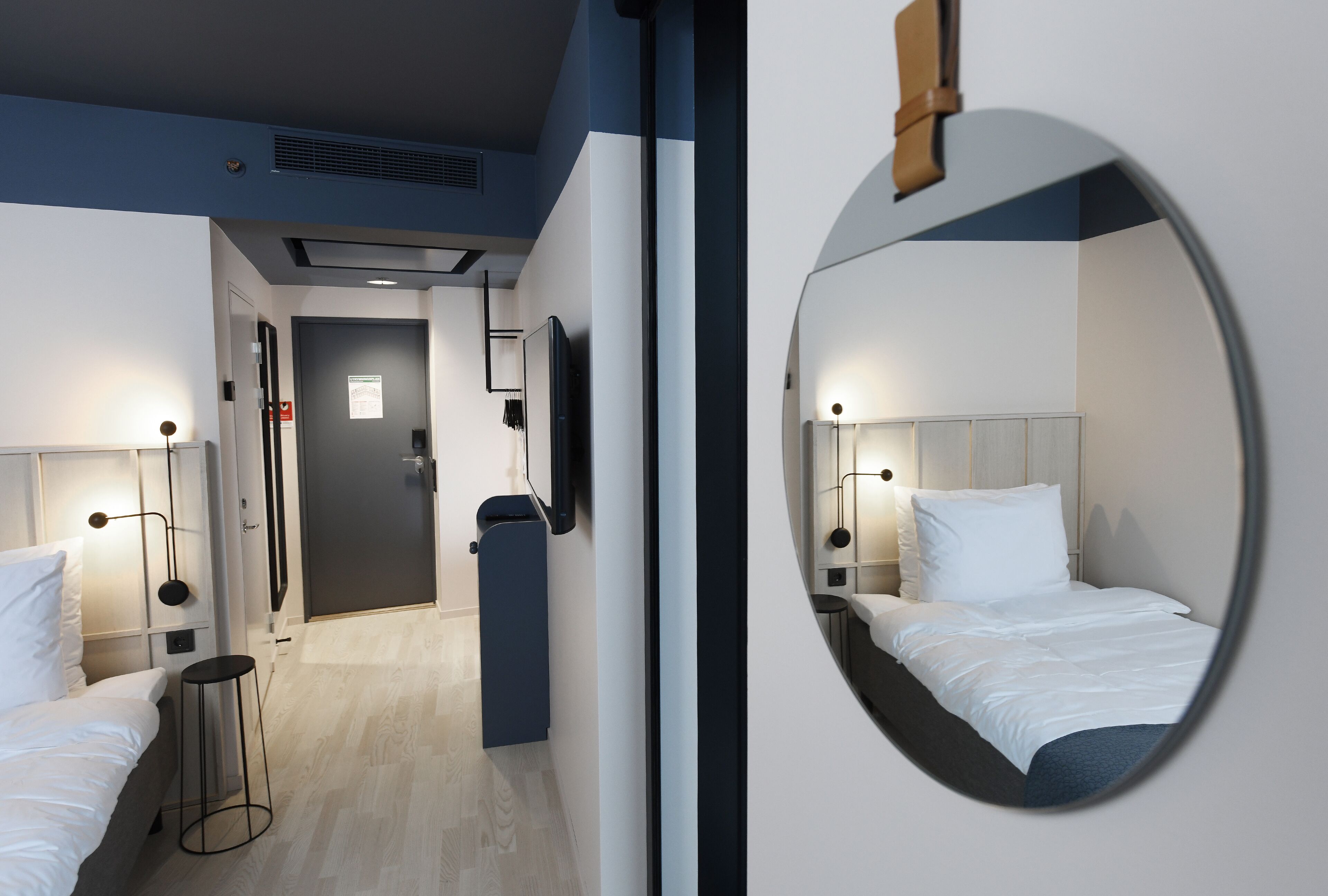 A modern hotel room with a large mirror, two beds, bedside tables, and a small stool.