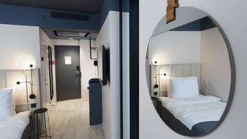 A modern hotel room with a large mirror, two beds, bedside tables, and a small stool.