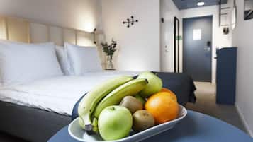 A hotel room with a bed, a bedside table with a fruit bowl, and a door in the background.