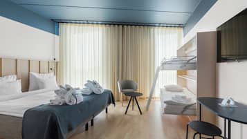 Habitación de hotel con cama, escritorio, silla, televisor y ventana con cortinas.