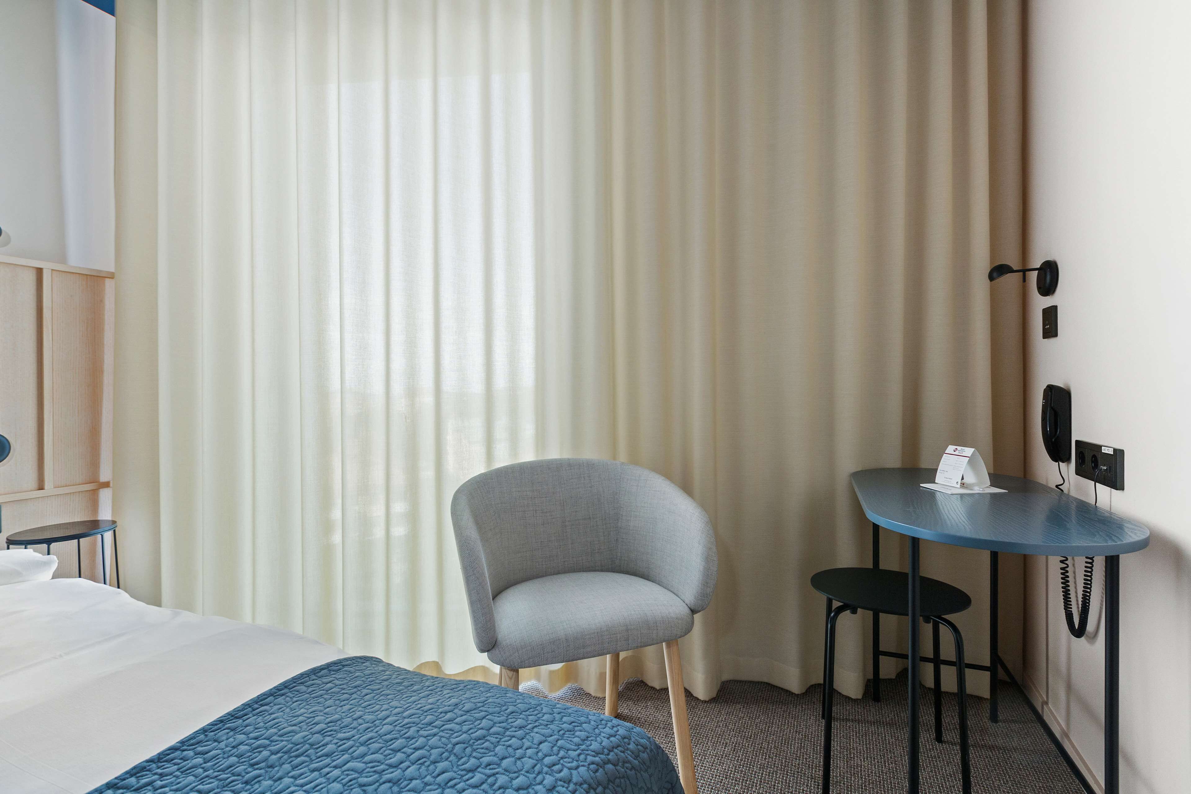 Ein Hotelzimmer mit Bett, Stuhl, kleinem Tisch und Telefon.