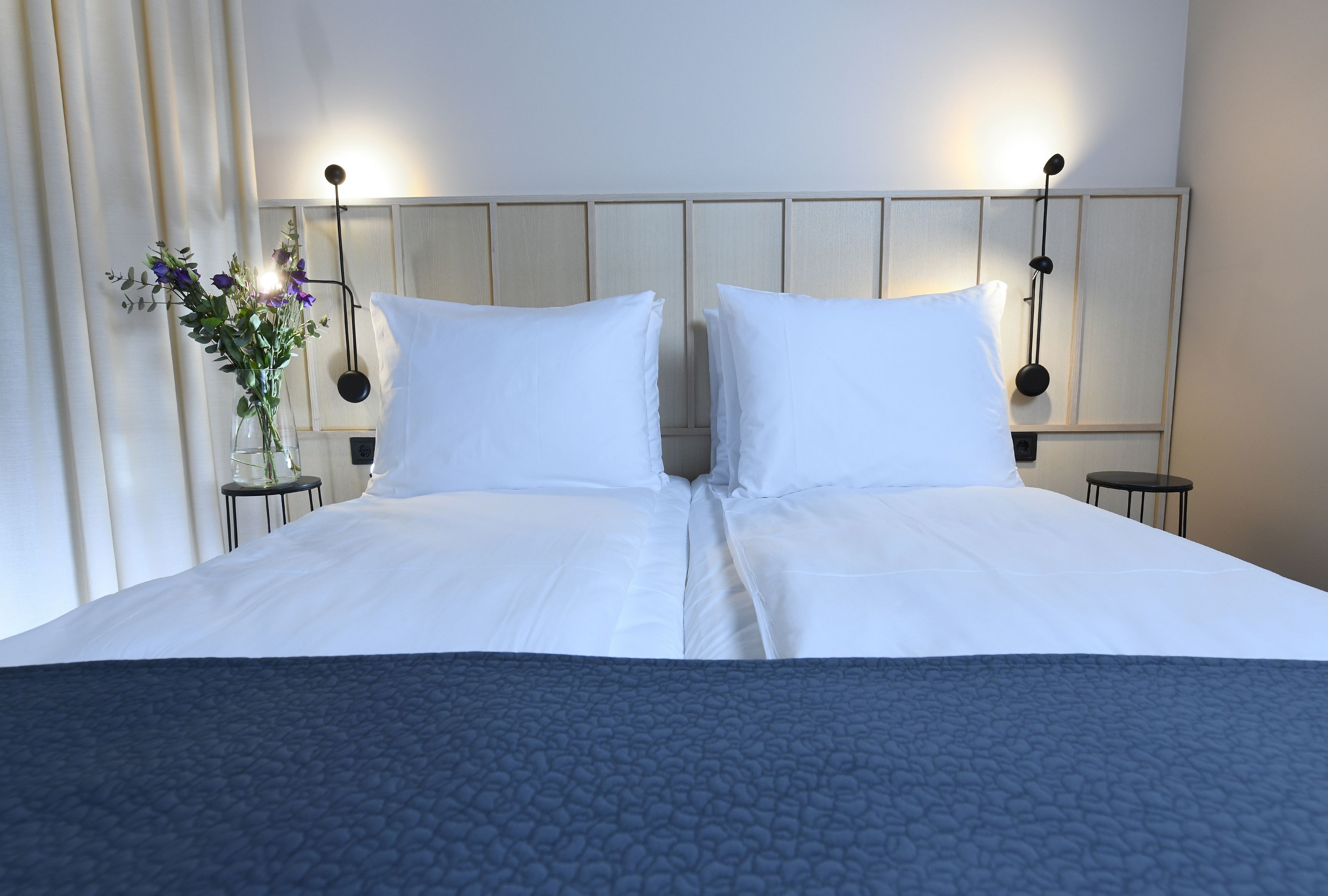 A double bed with white linens, a dark blue textured bedspread, and two bedside tables with lamps.