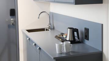 Una cucina compatta con lavandino, moka e due tazze bianche sul piano di lavoro.