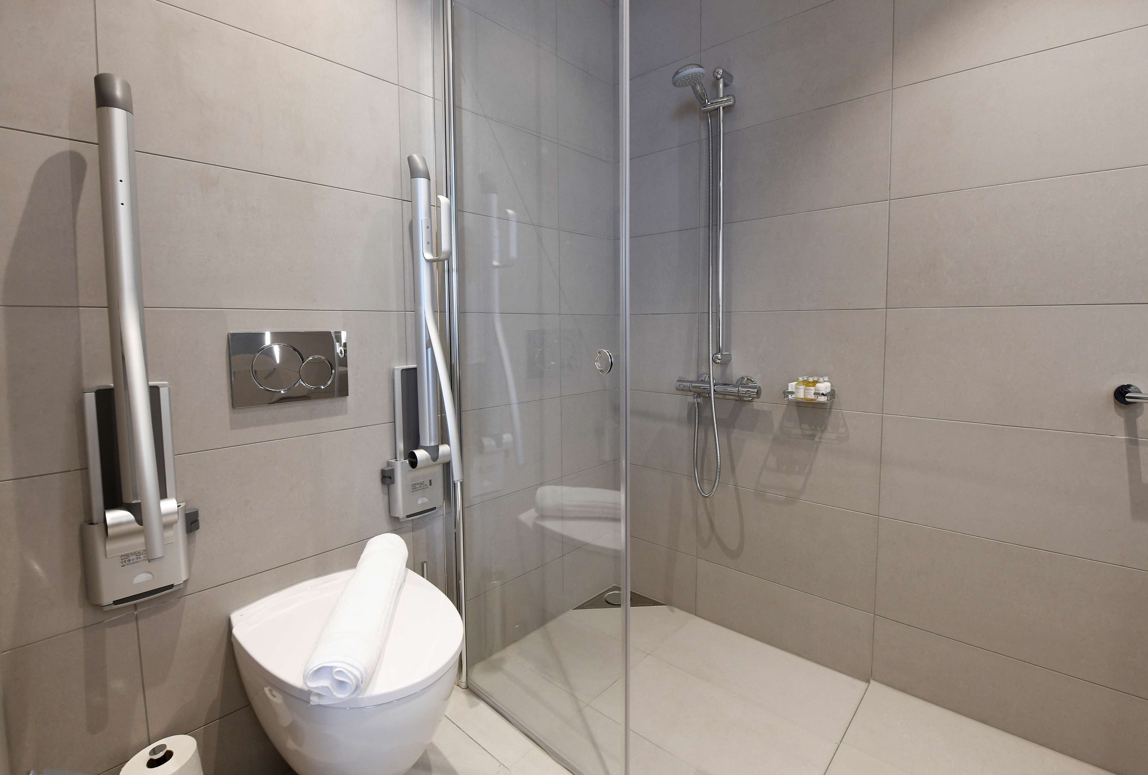 A modern bathroom with a glass-enclosed shower, a toilet, and a hand dryer.