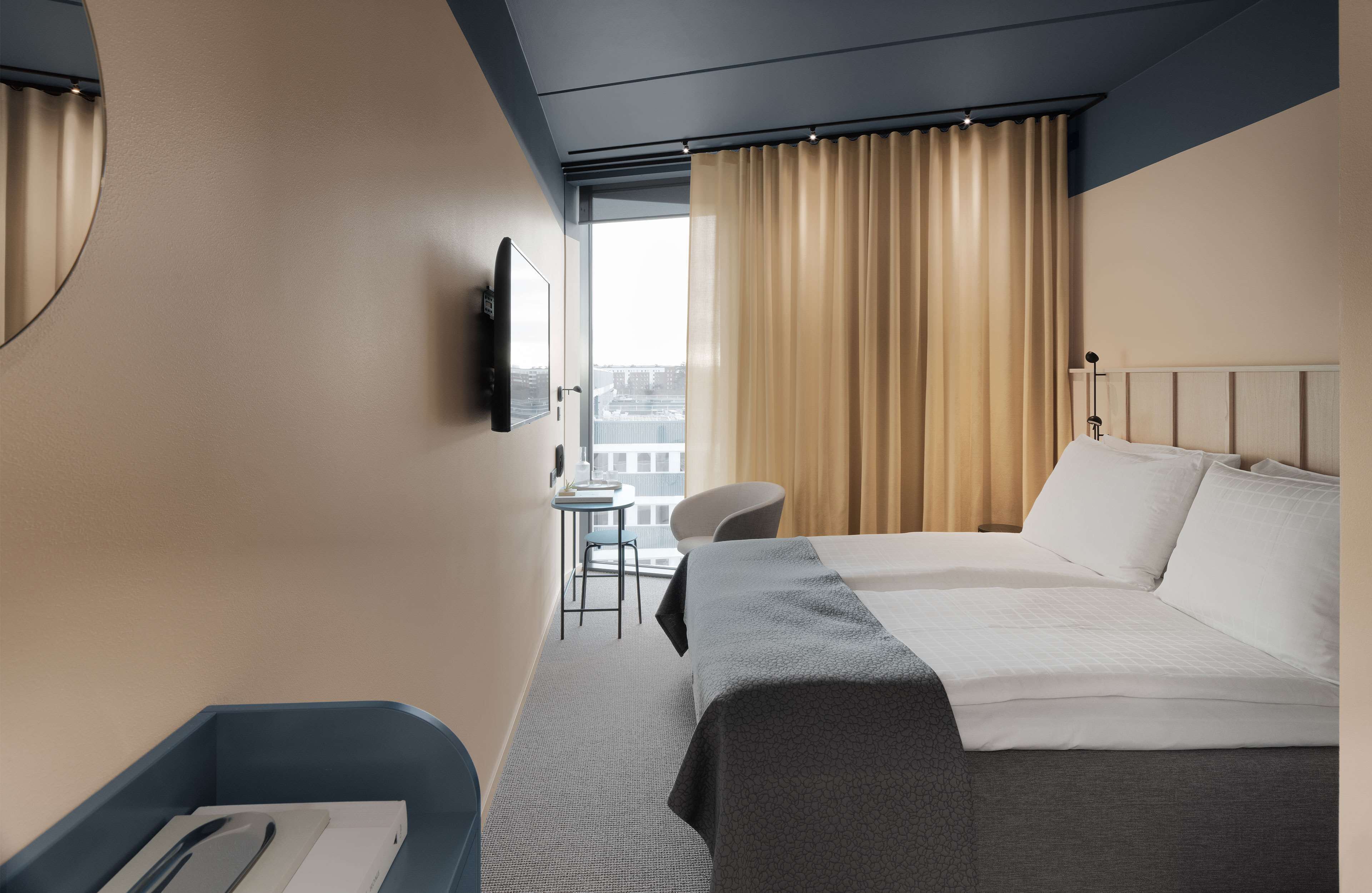 A hotel room with a bed, a desk, a chair, a TV, and a window with curtains.