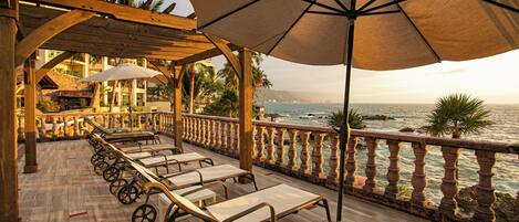 A wooden deck with sun loungers and umbrellas overlooking the ocean.