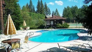 Une piscine entourée d’arbres, avec des chaises longues et des parasols, et un bâtiment sur lequel on peut voir une enseigne.