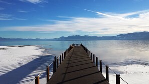 Un muelle de madera que se adentra en un lago tranquilo, con orillas nevadas y montañas al fondo.