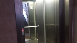 Un ascensor con interior metálico y puerta de cristal, que da acceso a una escalera.