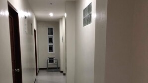 A narrow, well-lit hallway with white walls and a tiled floor, leading to a staircase with a small landing area. - Golite Hostel (Legazpi)