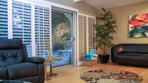 Un salon comprenant un canapé, une table basse en verre, un tapis à motifs, une plante en pot et une porte-fenêtre coulissante donnant sur un jardin.