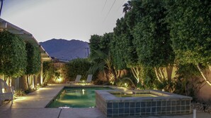 Une piscine avec un jacuzzi, entourée d’arbres et avec une montagne en toile de fond.