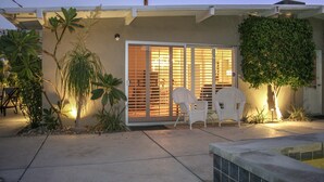 Une maison avec un patio, deux chaises blanches, un palmier et un petit jardin.