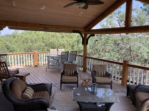 A covered outdoor deck with wicker furniture, a glass-top table, and a view of a forested area. - Spa style log cabin retreat on Sandia Mountain (Cedar Crest)