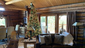 A cozy log cabin interior with a Christmas tree, wooden furniture, and large windows. - Spa style log cabin retreat on Sandia Mountain (Cedar Crest)