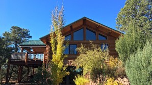 A two-story log cabin with a balcony, surrounded by a variety of trees and shrubs. - Spa style log cabin retreat on Sandia Mountain (Cedar Crest)