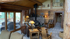 A cozy log cabin interior with a stone fireplace, wooden furniture, and a balcony with wicker chairs. - Spa style log cabin retreat on Sandia Mountain (Cedar Crest)