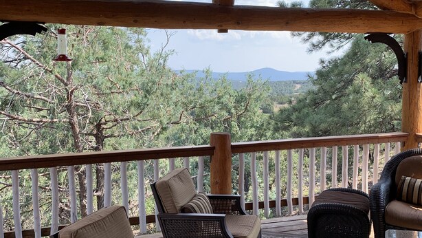 A covered outdoor seating area with wicker furniture and a view of trees and mountains. - Spa style log cabin retreat on Sandia Mountain (Cedar Crest)