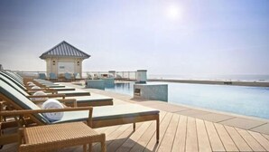 Un espace aménagé au bord de la piscine, avec des chaises longues et un petit pavillon offrant une vue sur l’océan.