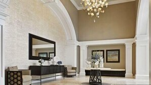 Un hall d’entrée spacieux avec un plafond haut, un grand miroir, un comptoir de réception et un espace salon.