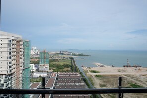 Ein Hochhaus mit mehreren Stockwerken, eine Baustelle inklusive Gerüst, und Blick auf eine Küstenlinie mit Strand und Meer.