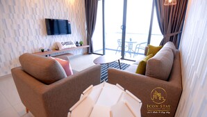 A modern living room with a sofa, armchairs, a TV, and a balcony with a table and chairs. - Atlantis Residence Iconstay Design Apartment by Iconstay Melaka (Malacca City)