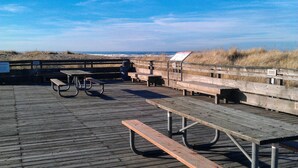 Een houten steiger met picknicktafels en bankjes met uitzicht op een strand.