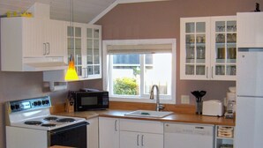 Een keuken met witte kasten, een houten tafel, een magnetron, een fornuis en een koelkast.