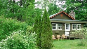 Une maison entourée d’une végétation luxuriante, dotée d’un porche bien visible et d’une cheminée.