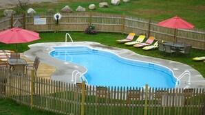 Une piscine entourée d’une clôture en bois, avec des chaises longues et des parasols.