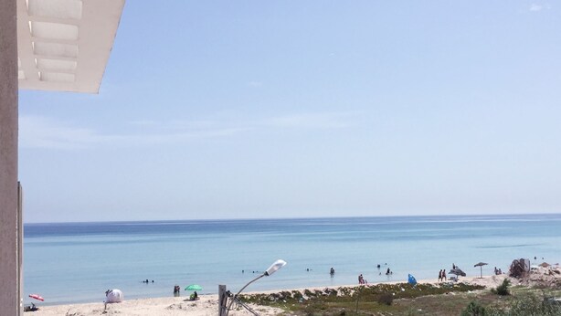 A beach view with a clear sky, sandy beach, and a few umbrellas.