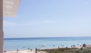 Vista da praia com céu claro, areia dourada e alguns guarda-sóis.