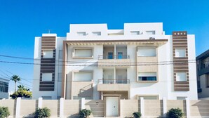 A modern multi-story residential building with balconies, a flat roof, and a gated entrance.