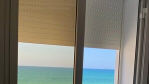 A view of a beach through a window with blinds.