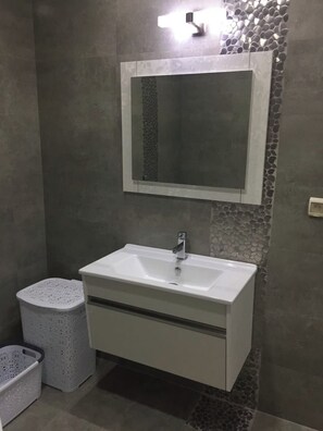 A bathroom with a white sink, a mirror above it, and a laundry basket to the left.