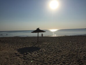 A beach with a thatched umbrella and footprints in the sand.