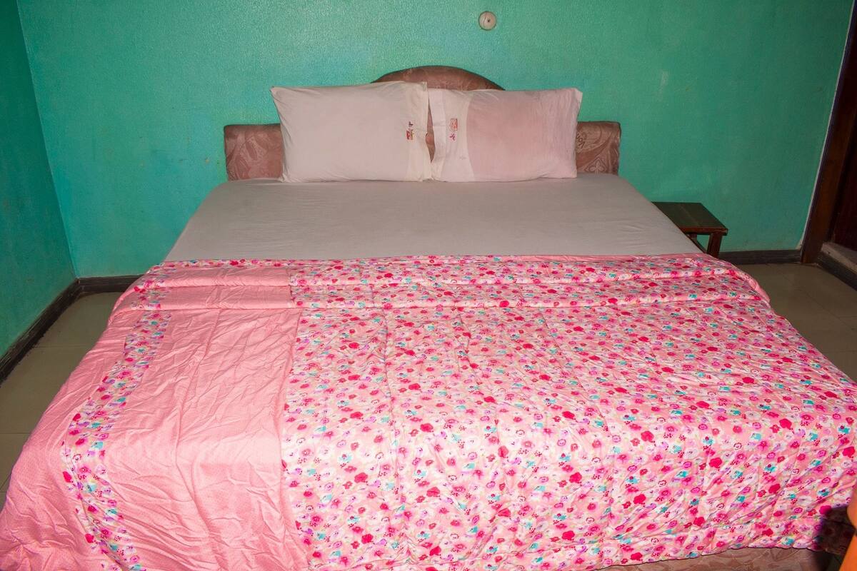 A bed with a floral bedspread and pillows, a wooden headboard, and a small bedside table.