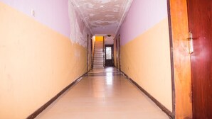 A long, narrow hallway with a wooden door on the right, a staircase at the end, and walls painted in two colors. - Jolac Hotel And Suites (Lagos)