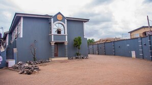 A building with a central entrance, a small tree in front, and a paved area. - Jolac Hotel And Suites (Lagos)