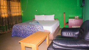 A room with a bed, a wooden table, a black leather chair, and a green wall. - Jolac Hotel And Suites (Lagos)