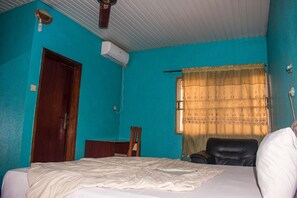 A room with teal walls, a bed, a desk, a chair, and a window with curtains. - Jolac Hotel And Suites (Lagos)