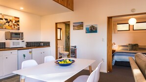 A compact living space with a kitchenette, a dining area with a bowl of fruit, a bed, and a view of the outdoors. - Allure Lodge cabin (Paihia)
